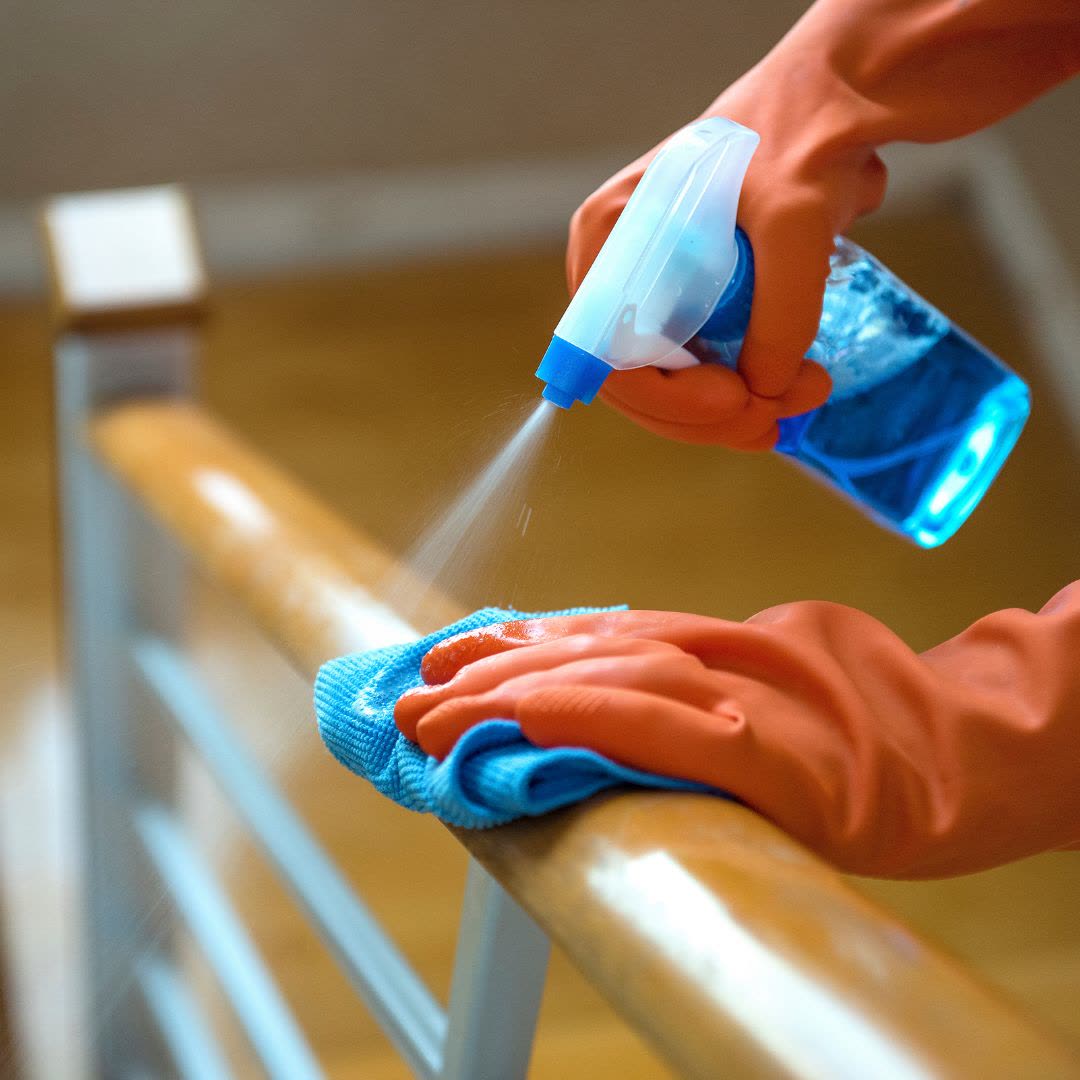Cleaner disinfecting a handrail in an office building