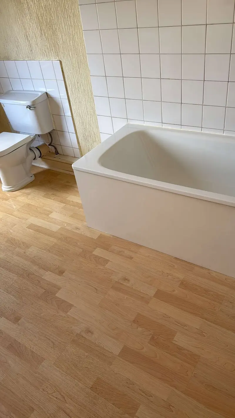 White bath, tiled wall and clean laminate floor in a bathroom