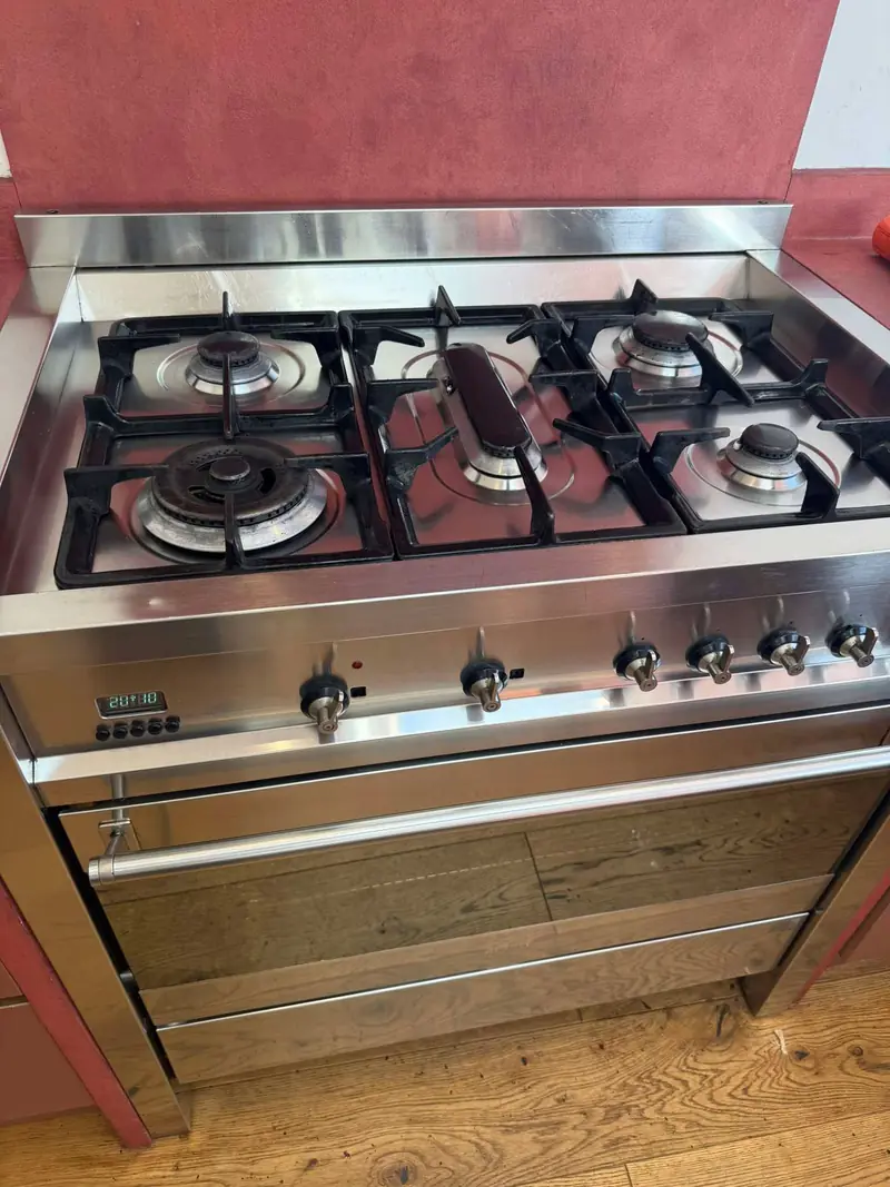 Stainless steel range cooker with a five-burner gas hob and cast iron pan supports