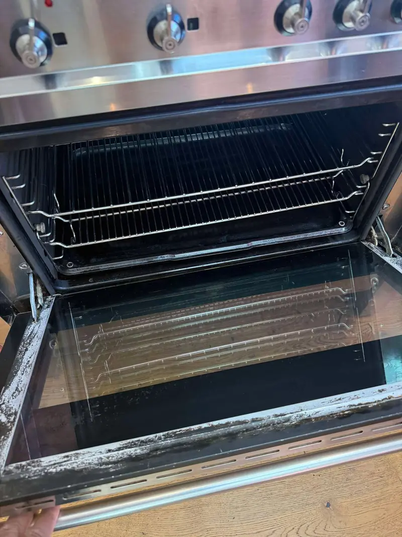 Stainless steel range cooker with the oven door open, showing a clean oven interior and shelves